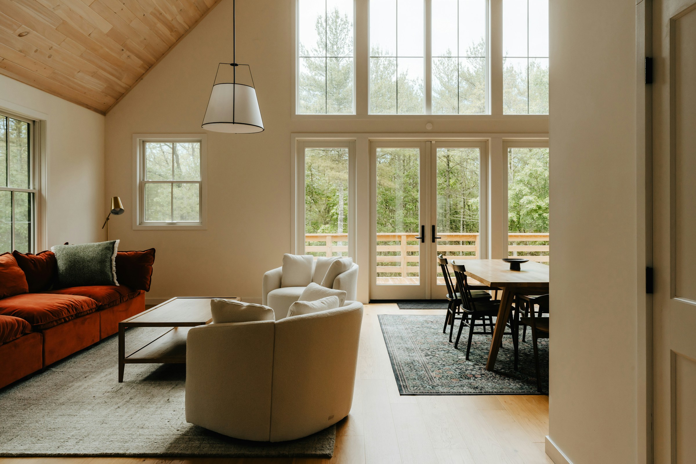 Salon rénové au plafond voûté en bois, canapé terracotta et grandes baies vitrées, lumière naturelle